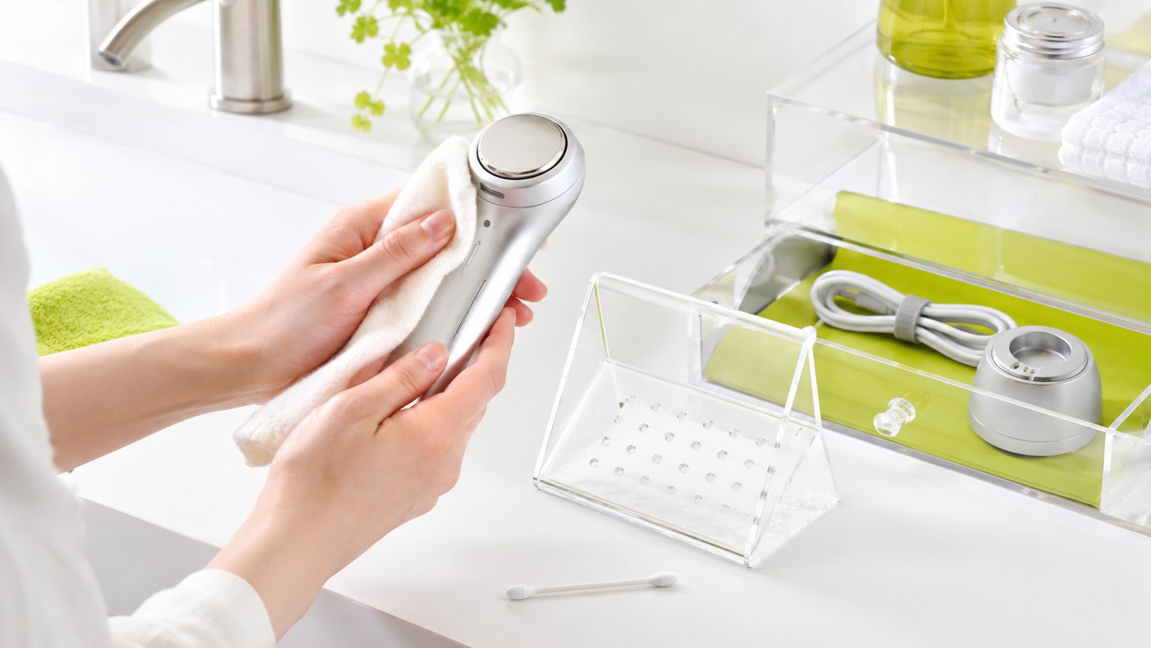 洗面台で美顔器を柔らかい布で拭き取り、付属品をケースに収納している手元
