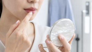 コンパクトミラーを見ながら指先でリップクリームを唇になじませている女性の口元