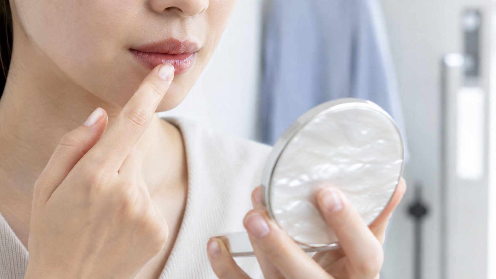 コンパクトミラーを見ながら指先でリップクリームを唇になじませている女性の口元